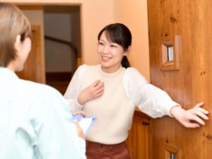 訪問する作業服の人物と玄関で扉を開ける若い女性